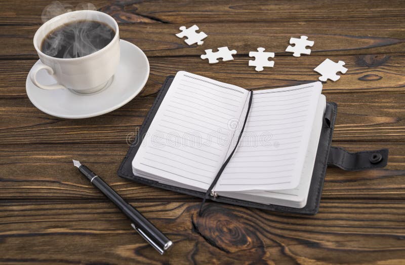 Notizbuch, Stift, Puzzlespiel und heißer Kaffee auf einem Holztisch lizenzfreies stockbild Notizbuch, Stift, Puzzlespiel und heißer Kaffee auf einem Holztisch lizenzfreies stockbild