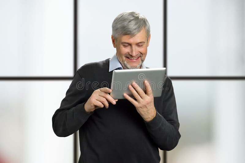 Notícia madura da leitura do sorriso do homem na tabuleta fotografia de stock royalty free Notícia madura da leitura do sorriso do homem na tabuleta fotografia de stock royalty free