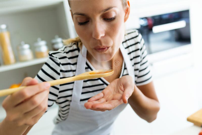 Nourriture à cuire et de soufflement de jeune femme en bonne santé avec la cuillère en bois dans la cuisine à la maison photos stock Nourriture à cuire et de soufflement de jeune femme en bonne santé avec la cuillère en bois dans la cuisine à la maison photos stock