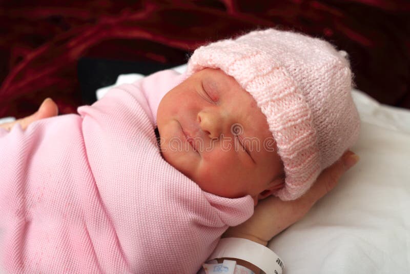 A close-up portrait of a sleeping bundled newborn baby wearing a pink knitted cap. Shallow depth of field. A close-up portrait of a sleeping bundled newborn baby wearing a pink knitted cap. Shallow depth of field.