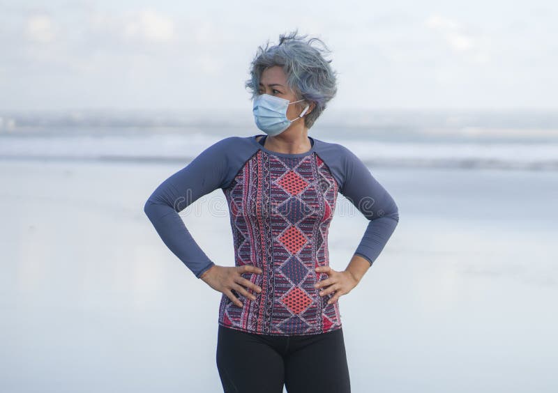 New normal running workout with face mask - attractive and happy middle aged woman on her 40s or 50s ready for post quarantine jogging at beautiful beach in healthy lifestyle concept. New normal running workout with face mask - attractive and happy middle aged woman on her 40s or 50s ready for post quarantine jogging at beautiful beach in healthy lifestyle concept