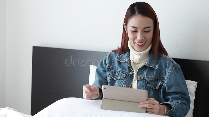Nouvelles visual observation de femme heureuse en ligne sur l'écran tactile au matin Fille asiatique en regardant dans la chambre banque de vidéos