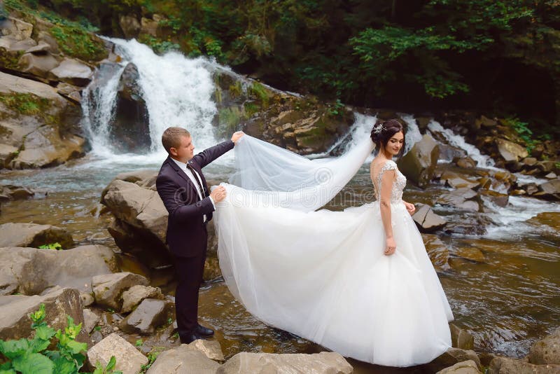 Novia Feliz Con El Novio Cerca De Una Cascada De La Montaña Vestido De Boda Lujoso Vida Del éxito Pares De La Boda Al Aire Libre Imagen de archivo - Imagen de Novia Feliz Con El Novio Cerca De Una Cascada De La Montaña Vestido De Boda Lujoso Vida Del éxito Pares De La Boda Al Aire Libre Imagen de archivo - Imagen de