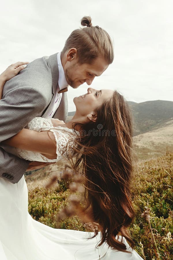 Novia feliz de la tenencia feliz elegante del novio en luz y la sonrisa del sol imagenes de archivo Novia feliz de la tenencia feliz elegante del novio en luz y la sonrisa del sol imagenes de archivo