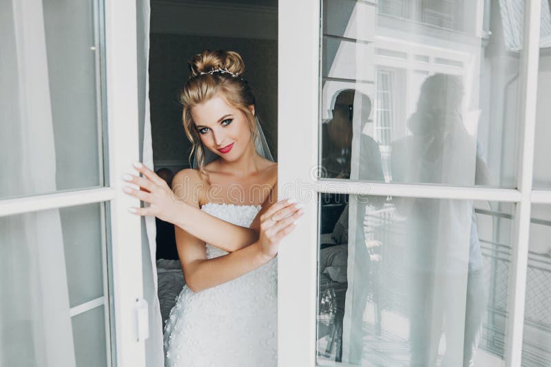 Novia feliz elegante que presenta y que sonríe en luz suave cerca de balcón de la ventana en la habitación Retrato sensual magníf imagenes de archivo Novia feliz elegante que presenta y que sonríe en luz suave cerca de balcón de la ventana en la habitación Retrato sensual magníf imagenes de archivo