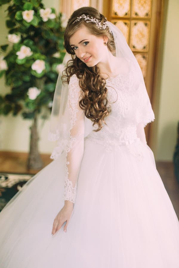 https://thumbs.dreamstime.com/b/novia-hermosa-en-vestido-de-boda-blanco-elegante-y-velo-con-el-pelo-rizado-largo-que-presenta-dentro-70956643.jpg