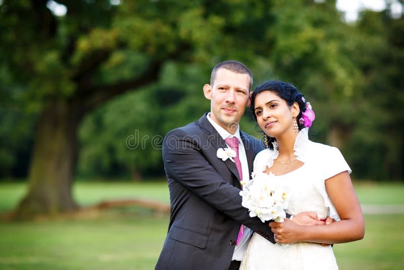 Novia india hermosa y novio caucásico, en parque del verano Flores felices de la explotación agrícola de la mujer joven Hombre jo fotografía de archivo libre de regalías Novia india hermosa y novio caucásico, en parque del verano Flores felices de la explotación agrícola de la mujer joven Hombre jo fotografía de archivo libre de regalías