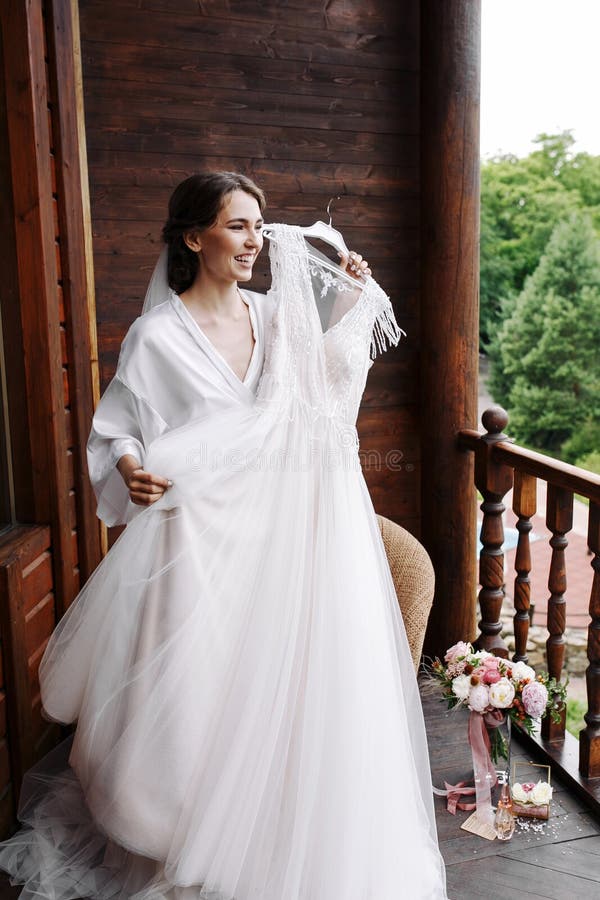 Novia magnífica, feliz de la sonrisa que goza del vestido de boda antes de llevar Preparaciones de la mañana Mujer que pone en el fotos de archivo libres de regalías Novia magnífica, feliz de la sonrisa que goza del vestido de boda antes de llevar Preparaciones de la mañana Mujer que pone en el fotos de archivo libres de regalías
