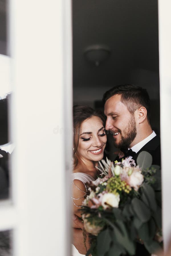 Novia magnífica y novio elegante que abrazan suavemente en la ventana Feliz imagen de archivo Novia magnífica y novio elegante que abrazan suavemente en la ventana Feliz imagen de archivo