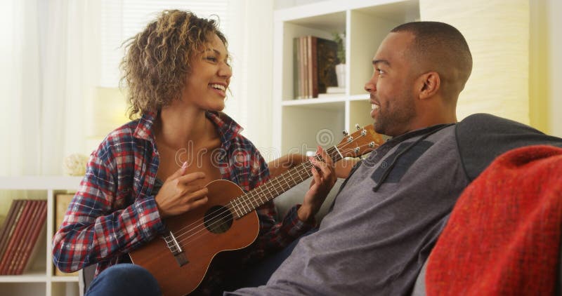 Novia negra linda serenading su novio con el ukelele foto de archivo Novia negra linda serenading su novio con el ukelele foto de archivo