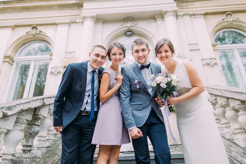 Novia y novio del recién casado con el padrino de boda feliz más la dama de honor que presenta en las escaleras del edificio clás imagen de archivo Novia y novio del recién casado con el padrino de boda feliz más la dama de honor que presenta en las escaleras del edificio clás imagen de archivo