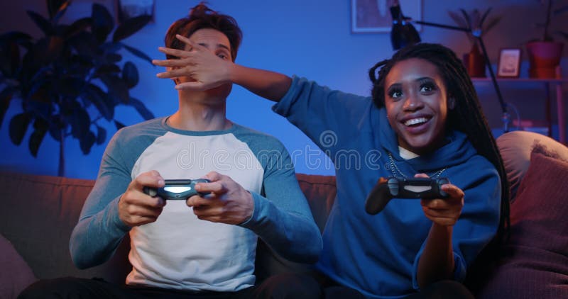 Novio feliz y novia jugando videojuegos y cargando joysticks en casa. la pareja milenaria disfrutando del juego mientras metrajes