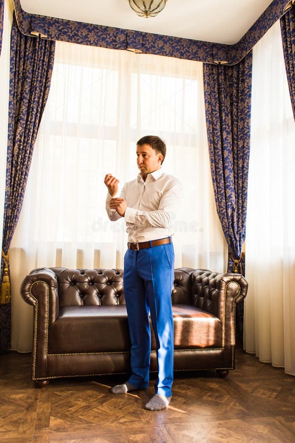 Novio hermoso magnífico feliz que consigue listo vestido por la mañana en fondo de un cuarto foto de archivo Novio hermoso magnífico feliz que consigue listo vestido por la mañana en fondo de un cuarto foto de archivo