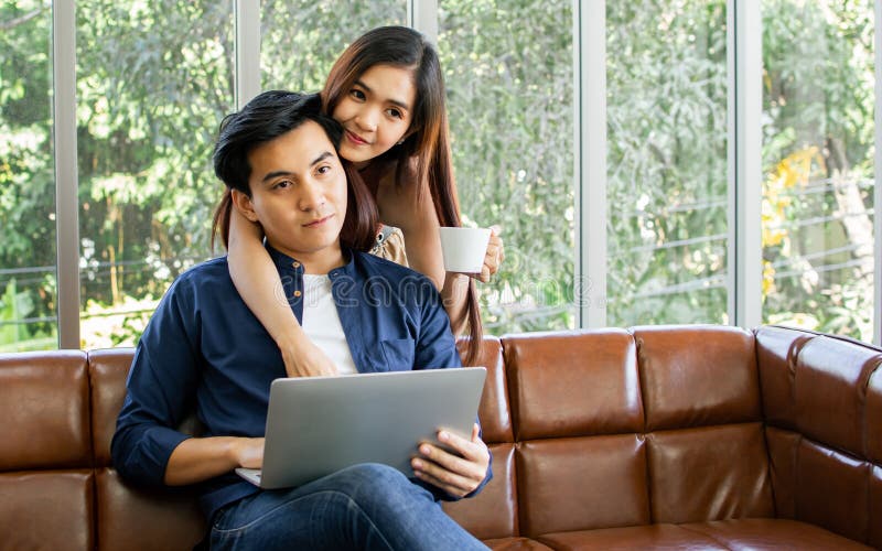 Novio y novia de pareja asiática sentada en un sofá en una acogedora sala de estar en casa por la mañana tomando café juntos y fotos de archivo