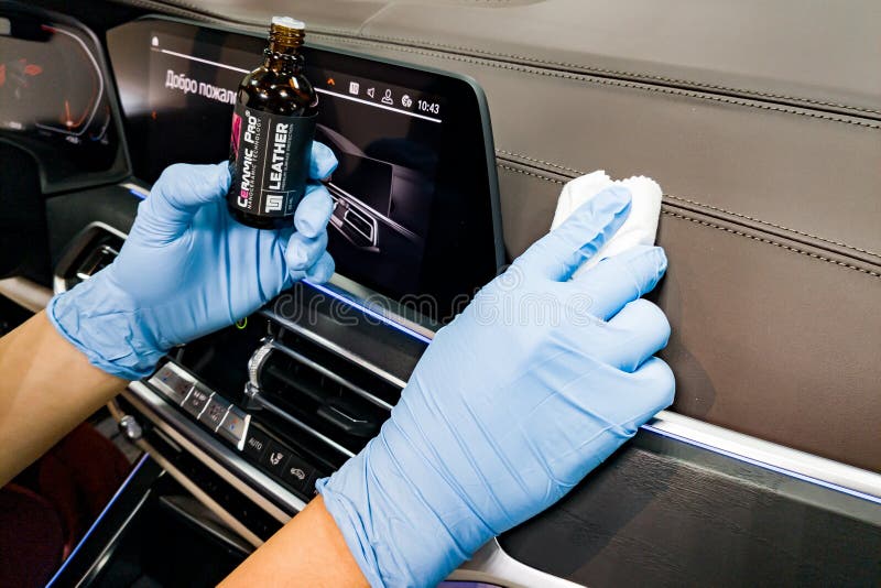 Applying a nano-ceramic coating for interior Ceramic Pro Leather 9h and Light on the car dashboard brown upholstery by a worker