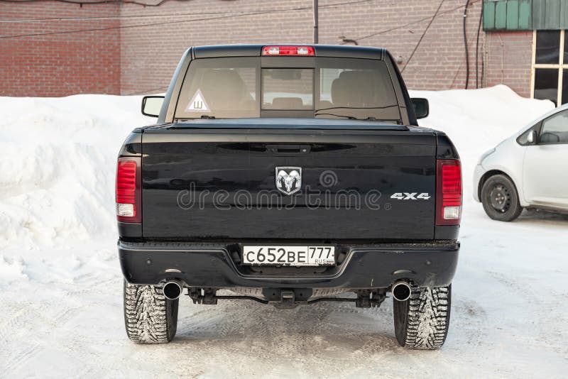 Black Dodge Ram with an engine of 5.7 liters rear view with two exhaust pipes on the car parking with snow background