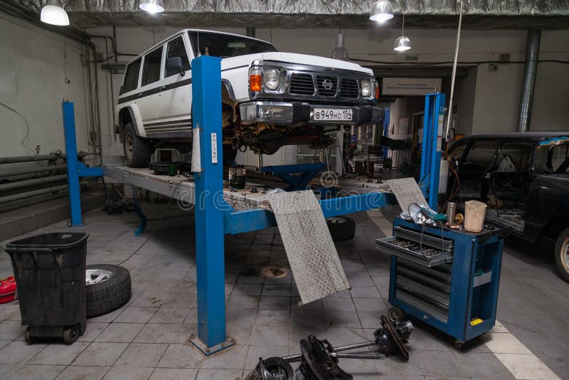 White used car Nissan Patrol raised on a blue lift for repairing the chassis and engine in a vehicle repair shop. Auto service royalty free stock photography White used car Nissan Patrol raised on a blue lift for repairing the chassis and engine in a vehicle repair shop. Auto service royalty free stock photography
