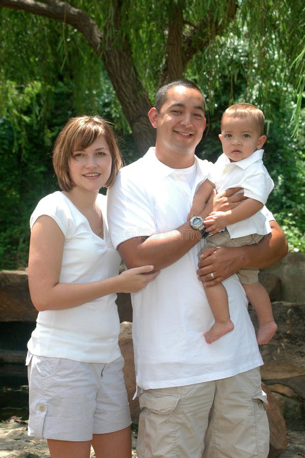 Young married couple with their toddler child. New family taking pictures in white shirts and tan shorts. Family of three. Young married couple with their toddler child. New family taking pictures in white shirts and tan shorts. Family of three.