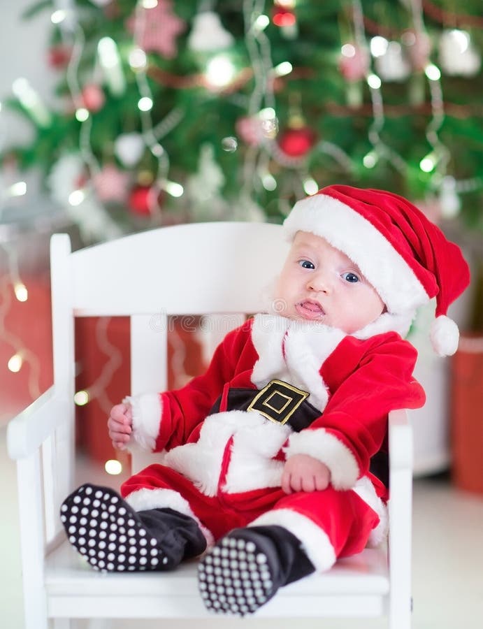 Nowonarodzona chłopiec w Santa stroju obsiadaniu pod Chr zdjęcie stock Nowonarodzona chłopiec w Santa stroju obsiadaniu pod Chr zdjęcie stock