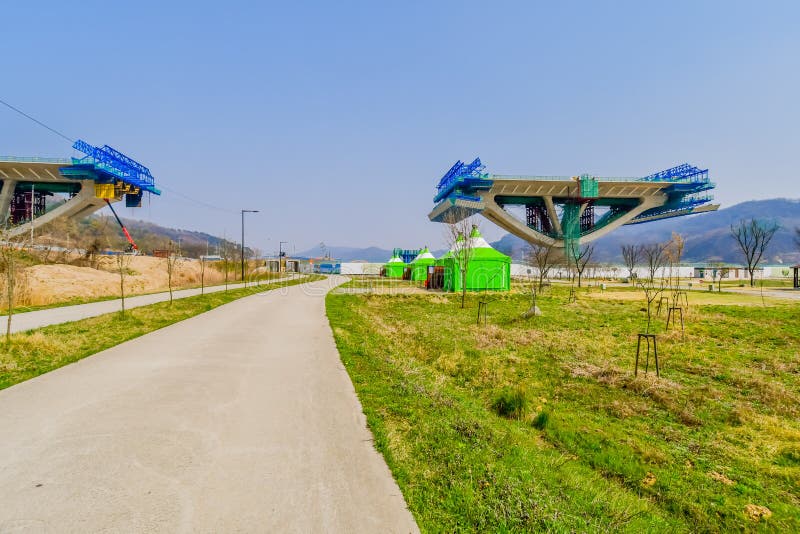 Sejong, South Korea; April 1, 2020: Landscape of public park with green tents near sidewalk and side view of new bridge under construction. Sejong, South Korea; April 1, 2020: Landscape of public park with green tents near sidewalk and side view of new bridge under construction