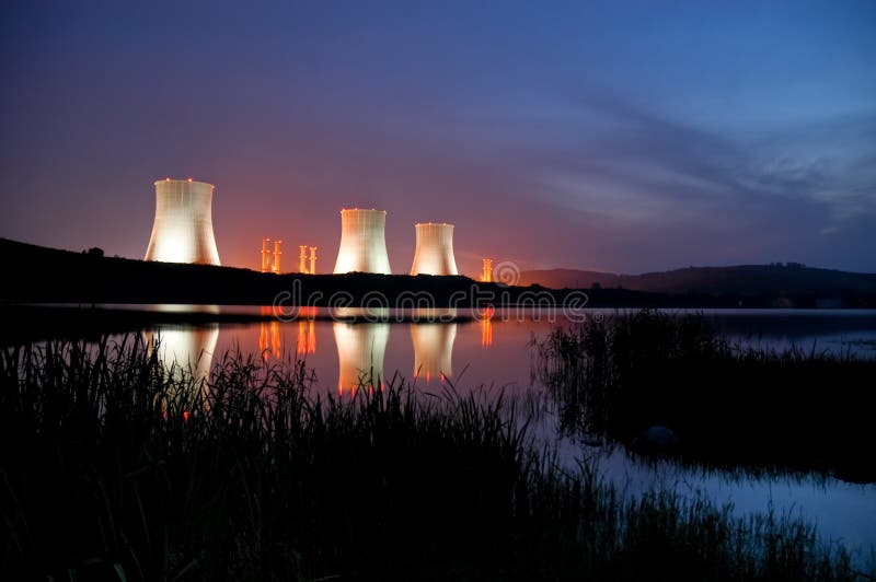 Nucleare torri di raffreddamento che di notte è illuminato con pittoresco lago in primo piano.