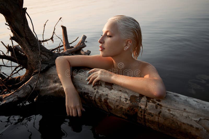 Nude naked sexy woman in water at sunset. Beautiful blonde woman with short wet hair and big breasts, art portrait in sea