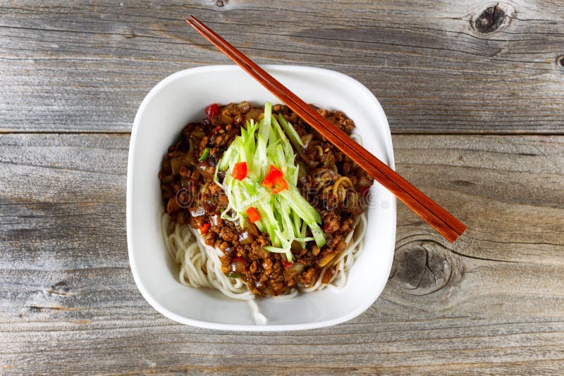 High angled view of noodles with ground beef and cucumbers. Chopsticks on top of bowl with rustic wood underneath. High angled view of noodles with ground beef and cucumbers. Chopsticks on top of bowl with rustic wood underneath.