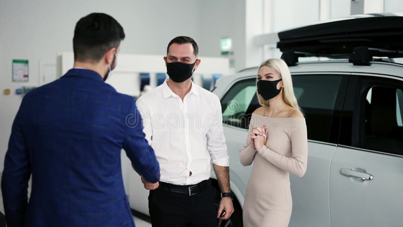 Nuevos propietarios de autos que reciben las llaves de un auto de lujo comprado en el concesionario usando máscaras metrajes