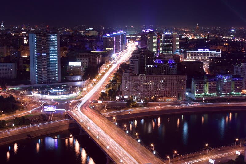 Modern contemporary Russian architecture cityscape: Aerial view from above of night megalopolis / city Moscow (Russia) at night / evening with buildings, alight street, streetlight, bridge, river with reflections and traffic - cars look like red and white light trails. Modern contemporary Russian architecture cityscape: Aerial view from above of night megalopolis / city Moscow (Russia) at night / evening with buildings, alight street, streetlight, bridge, river with reflections and traffic - cars look like red and white light trails.