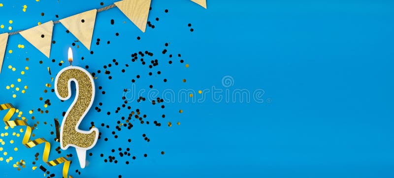 Number 2 gold celebration candle on star and glitter blue background. Copy space. Banner