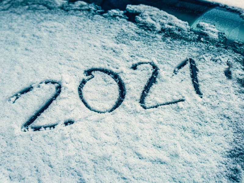 The numbers of the New Year 2021 are written on the snow-covered glass of the car. Travel route concept in winter season