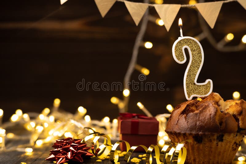 Number 2 gold burning candle in a cupcake against celebration wooden background with lights. Birthday cupcake. Copy space. Banner. Number 2 gold burning candle in a cupcake against celebration wooden background with lights. Birthday cupcake. Copy space. Banner