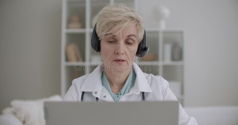 Numirea online cu o femeie în vârstă cu experiență în medicina muncii comunică online cu pacientul sau colegul stock footage