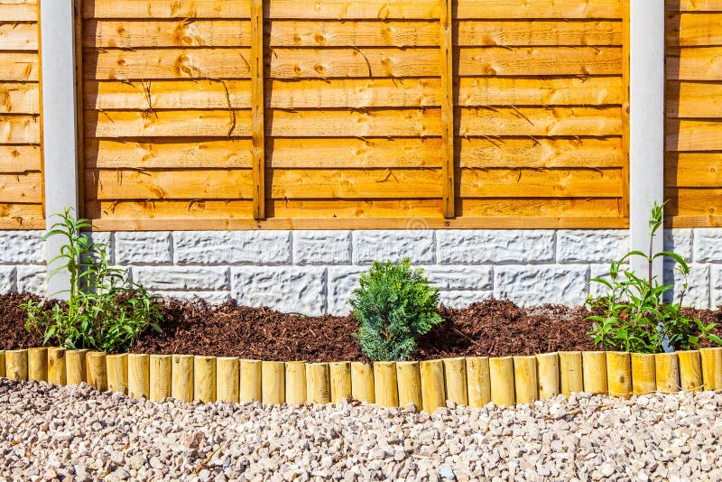 New landscaped wood chip garden border with small wooden fence edging and plants. Concrete posts and gravel boards and timber fencing. New landscaped wood chip garden border with small wooden fence edging and plants. Concrete posts and gravel boards and timber fencing.