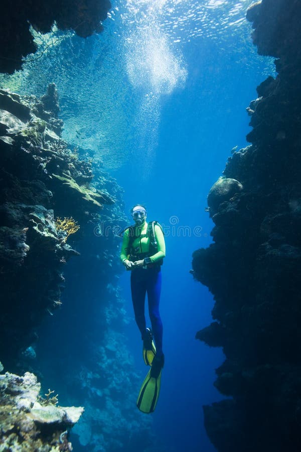 A pretty female scuba diver swimming between two coral cliffs, underwater. A pretty female scuba diver swimming between two coral cliffs, underwater