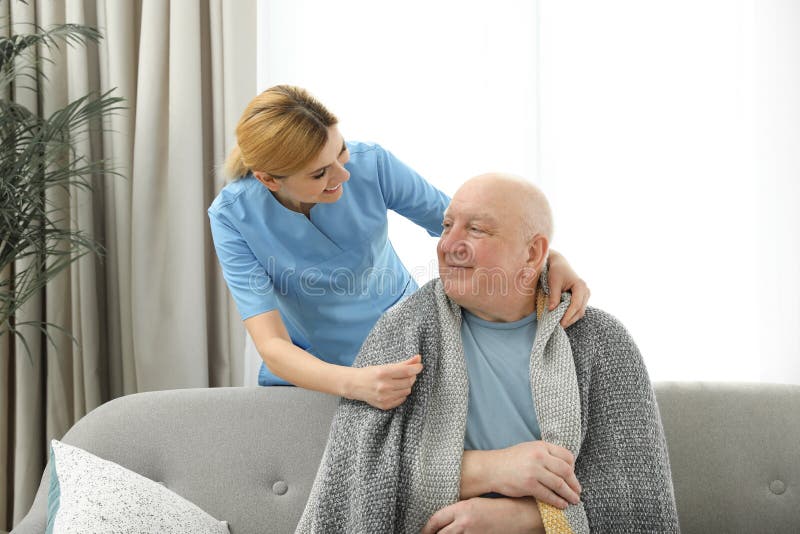 Nurse covering elderly man with blanket. Assisting senior people stock photo Nurse covering elderly man with blanket. Assisting senior people stock photo