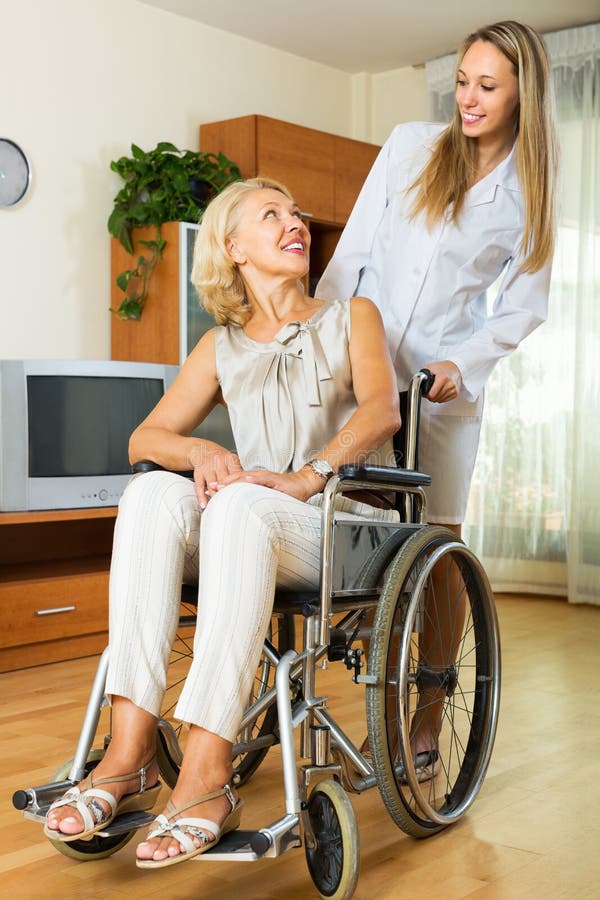 Friendly female nurse and disabled women on chair communicating indoor. Friendly female nurse and disabled women on chair communicating indoor