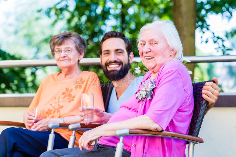 Nurse drinking coffee with seniors on terrace of retirement home