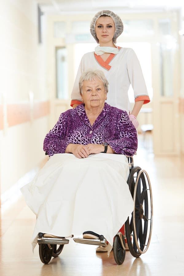 Female nurse carer and aged elderly patient women in wheelchair at clinic hallway. Female nurse carer and aged elderly patient women in wheelchair at clinic hallway