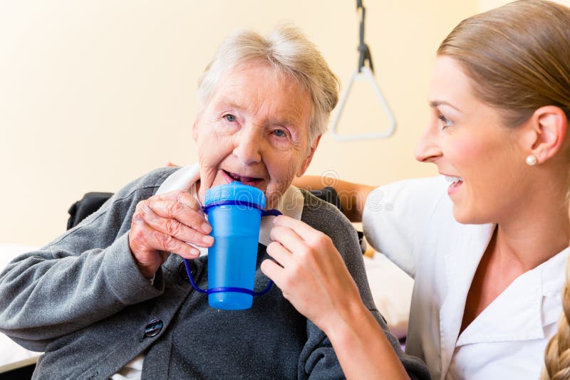 Nurse in nursing home giving drink to elderly women sitting in wheelchair. Nurse in nursing home giving drink to elderly women sitting in wheelchair