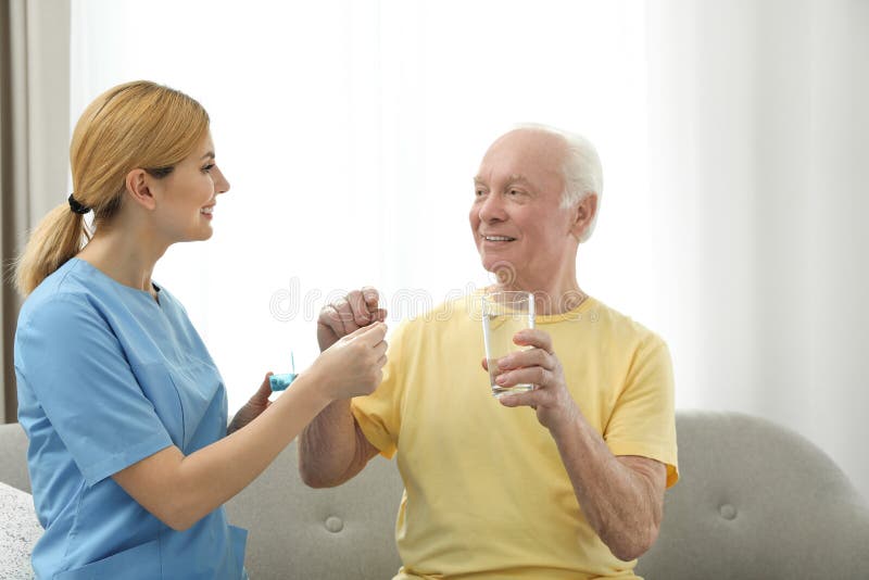 Nurse giving medication to elderly man indoors stock photography Nurse giving medication to elderly man indoors stock photography