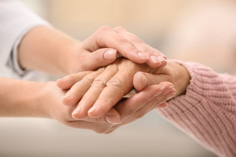 Nurse holding hands of elderly woman against blurred background. Assisting senior generation