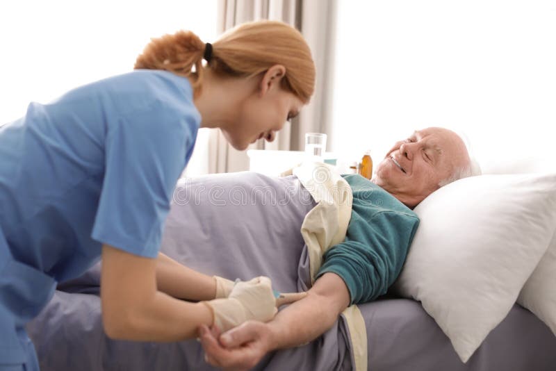 Nurse making injection to elderly man on bed. Medical assistance stock photography