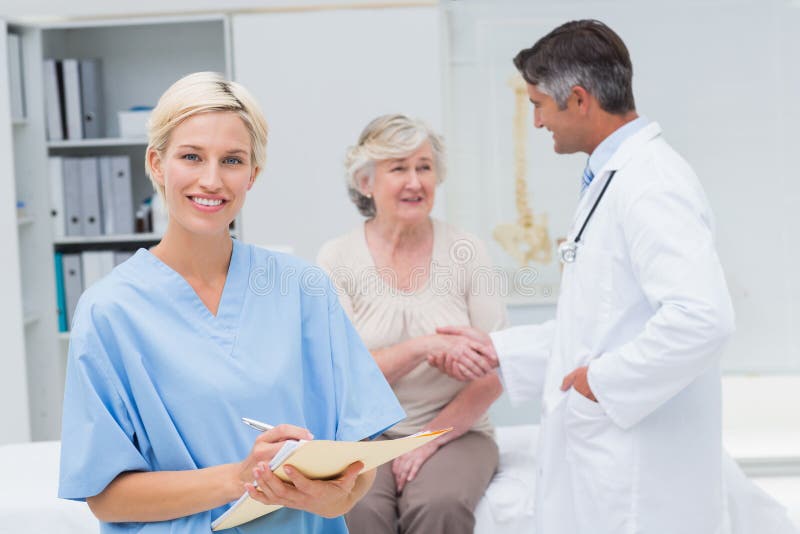 Nurse making reports while doctor and patient shaking hands stock image