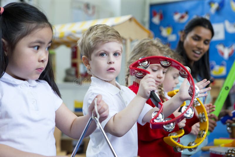 Nursery children playing with musical instruments in the classroom. One little boy is looking at the camera with a tambourine. Nursery children playing with musical instruments in the classroom. One little boy is looking at the camera with a tambourine.