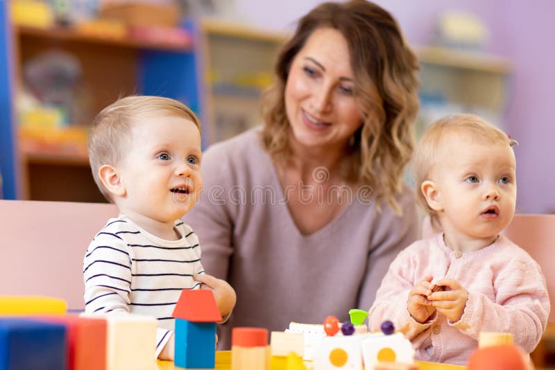 Nursery teacher looking after children in daycare. Little kids toddlers play together with developmental toys stock photos Nursery teacher looking after children in daycare. Little kids toddlers play together with developmental toys stock photos