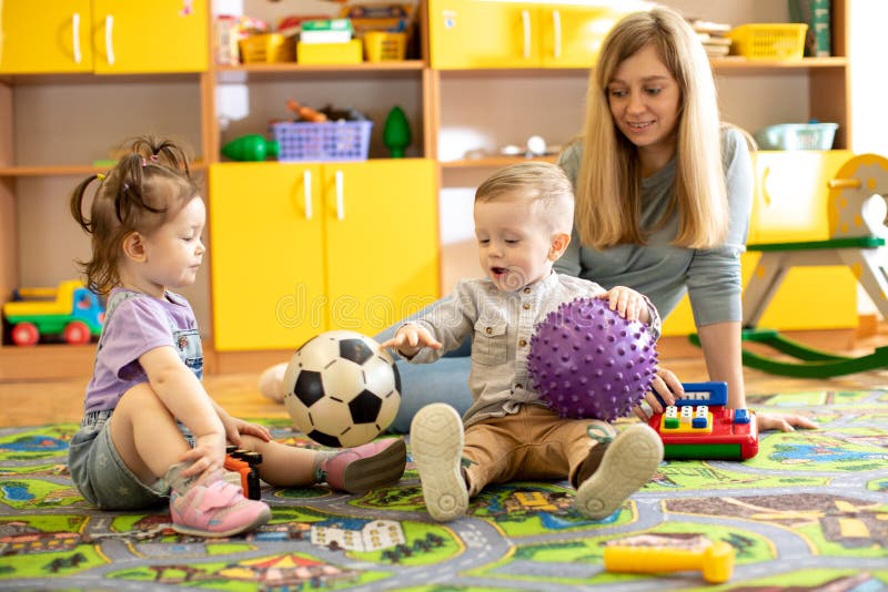 Nursery teacher looking after children in kindergarten. Little kids toddlers play together with toys. royalty free stock image Nursery teacher looking after children in kindergarten. Little kids toddlers play together with toys. royalty free stock image