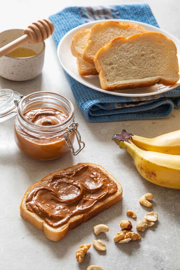 Nut butter toast with bananas and honey on light table. Walnut, hazelnut and cashew nut spread in glass jar.