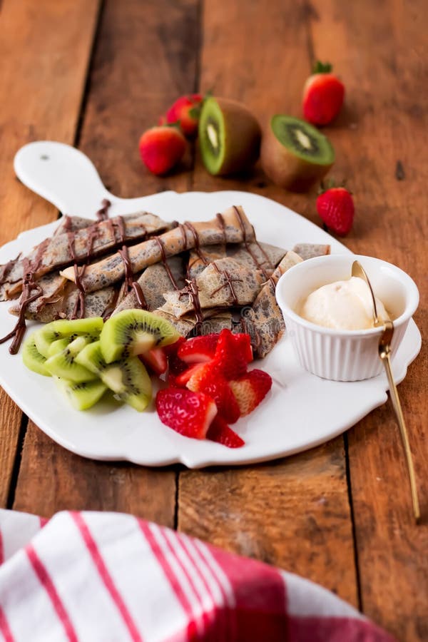 Nutella Crepes με κομμένες φράουλες kiwi και ένα κομμάτι παγωτό σερβίρεται σε λευκό πιάτο απομονωμένη ξύλινη πλαϊνή όψη στοκ εικόνα με δικαίωμα ελεύθερης χρήσης