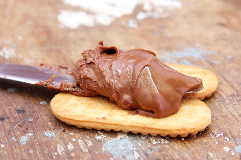 Photo of chocolate nutella on knife with biscuits on wooden background. Photo of chocolate nutella on knife with biscuits on wooden background
